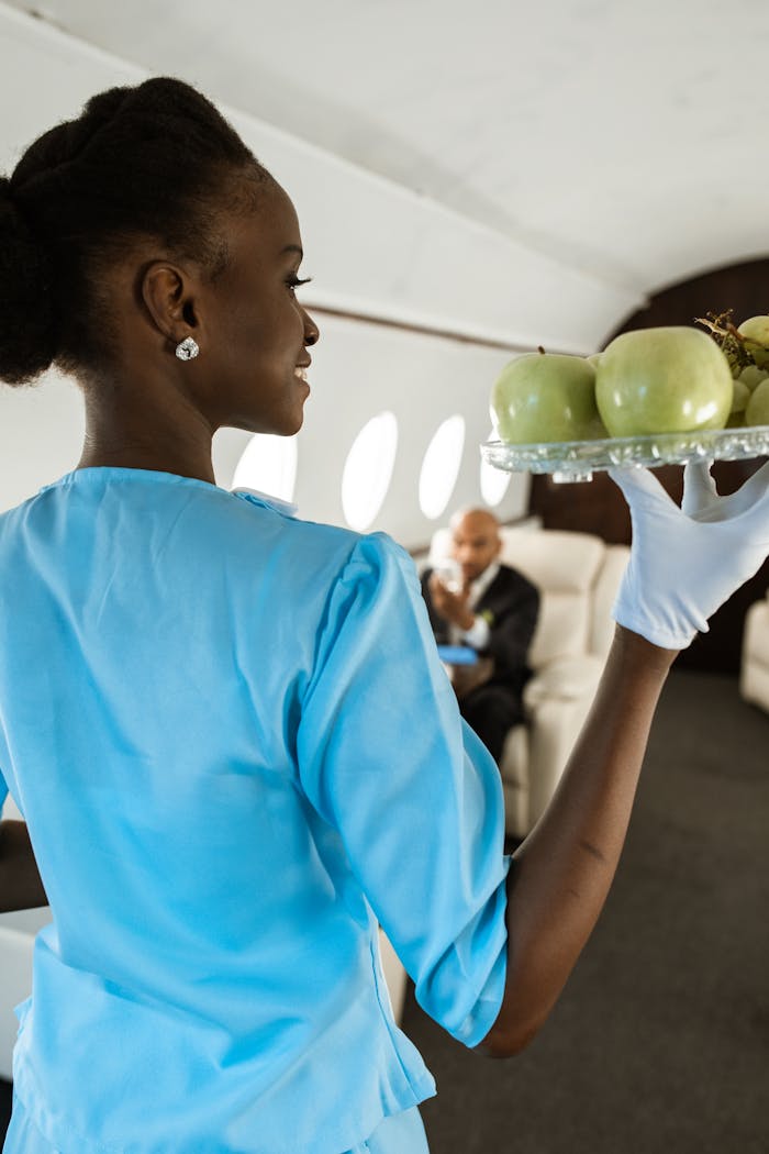 Flight attendant in blue uniform serving fruits aboard a luxury private jet interior.